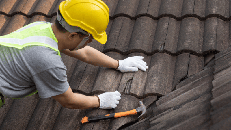 Roofing professional replacing damaged roof tiles on an older roof to restore weather protection and structural integrity.