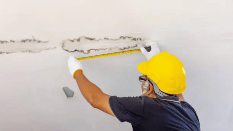 Contractor inspecting interior ceiling water damage caused by a leaking roof and prolonged moisture exposure.