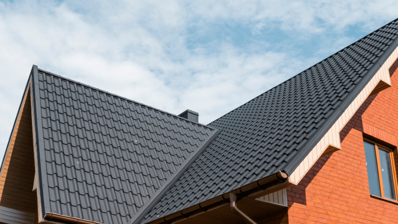 Worker installing metal roofing sheets using power tools during a residential metal roof installation project.