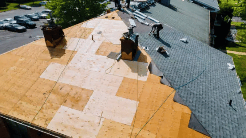 Roof installation in progress showing underlayment, exposed decking, and new shingles being applied by roofing professionals.