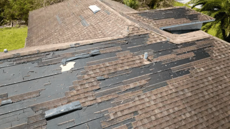 Severely damaged asphalt shingle roof with missing and torn shingles, exposing underlayment and increasing the risk of roof leaks.